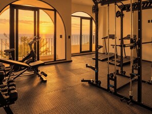 A gym with exercise equipment, large windows, and a view of the sunset. - Vista Vigía Loft · Ideal for 2 in Mazatlan (Mazatlán)