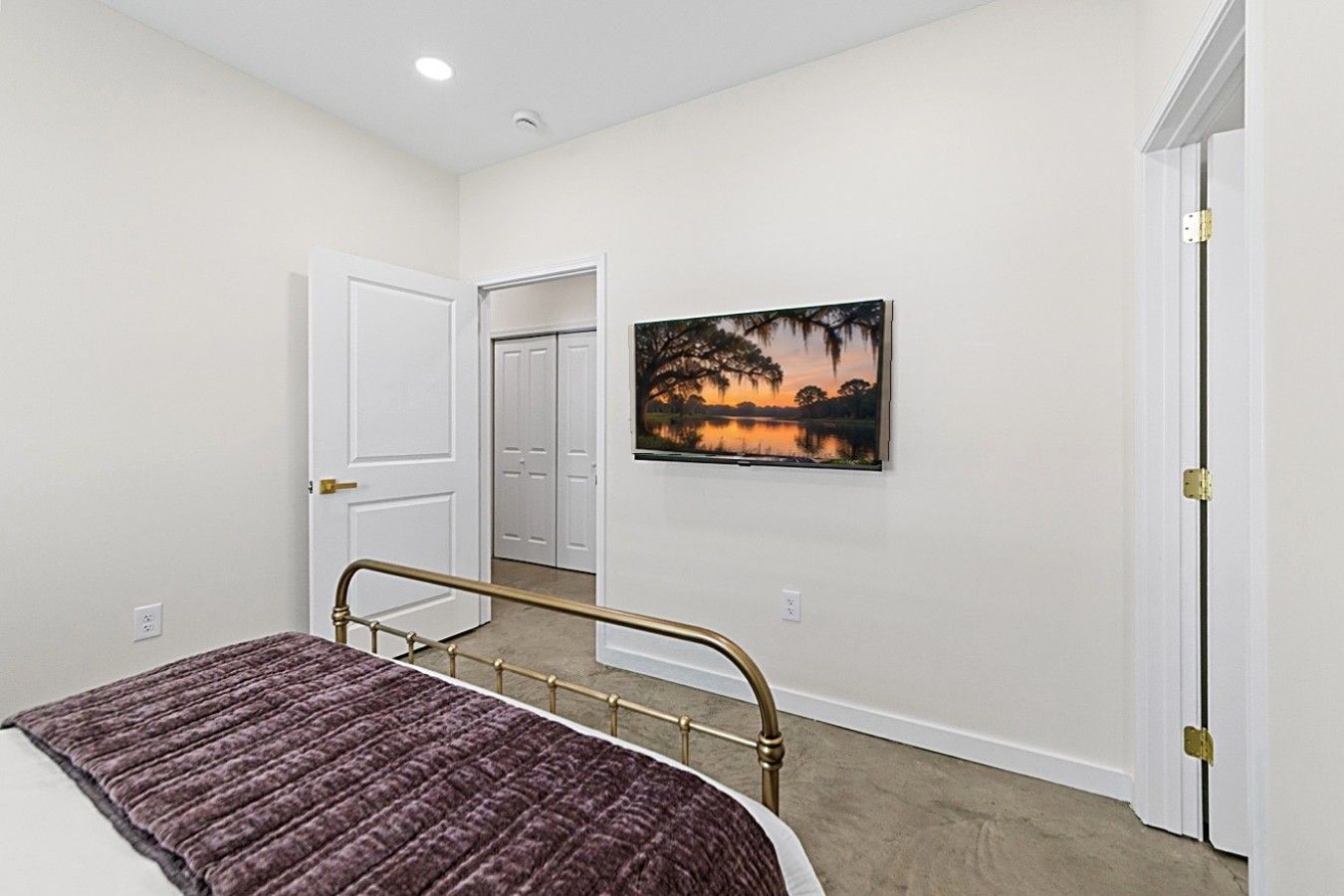 A bedroom with a bed, a door, a hallway, and a painting on the wall.