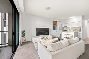 Een moderne woonkamer met een flatscreen televisie, een bank, een klein bijzettafeltje en een potplant.