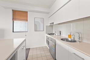 A modern kitchen with white cabinets, a stainless steel sink, a gas stove, and a dishwasher. - Elegant 2BR Escape with City Views | Brisbane CBD (Brisbane City)