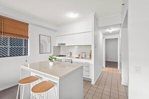 A modern kitchen with white cabinetry, a central island with stools, a window with blinds, and a tiled floor. - Elegant 2BR Escape with City Views | Brisbane CBD (Brisbane City)
