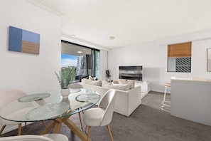 A modern apartment with a glass dining table, white sofas, a flat-screen TV, and a kitchen area. - Elegant 2BR Escape with City Views | Brisbane CBD (Brisbane City)