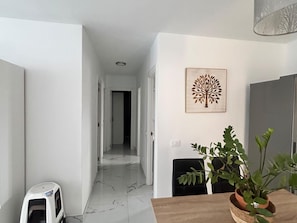 A hallway with a white floor, a door at the end, and a wall-mounted artwork. - San Eugenio Fantastic New 4 bedrooms wifi free (Costa Adeje)