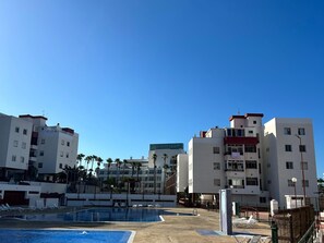 Et hotel med flere etager, en swimmingpool og palmer.