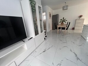 Een moderne woonkamer met een flatscreen televisie, een eethoek met tafel en stoelen, en een keuken met kasten en een koelkast.