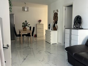 En moderne stue med spiseplads, et hvidt skab, en sort sofa og en loftsvifte.