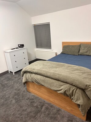 Un dormitorio con cama, cómoda, radiador y ventana con persianas.