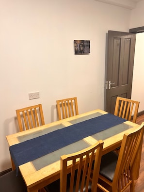 Un comedor con una mesa y sillas de madera, un mantel azul y un cuadro colgado en la pared.