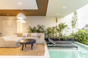 A modern living room with a sectional sofa, a round coffee table, and a poolside area with plants. - OriVista 2BR Private Pool Villa w/ Rice FieldView (Ubud)