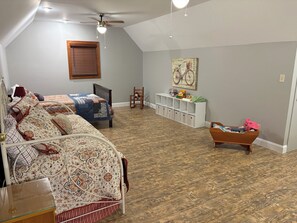 A spacious room with a sloped ceiling, a ceiling fan, a wooden rocking chair, a bed with patterned bedding, and a white storage unit with toys. - Quiet and Spacious 4-bedroom house in Ringgold...great for families! (Ringgold)