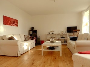 A living room with two white sofas, a coffee table, and a television on a white stand. - Holiday Apartment With 2 Bedrooms (Oldsum)