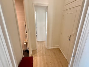 A narrow hallway with a wooden floor, white walls, and a door at the end. - Apartment Near Parc Fenestre (La Bourboule)