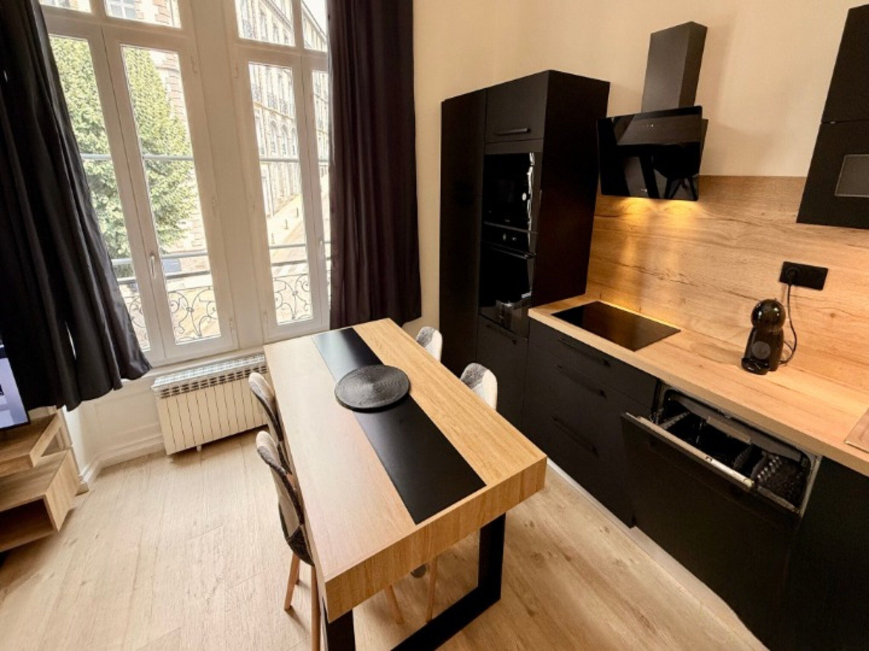 Una cocina moderna con una mesa de comedor, armarios negros y vistas al exterior.