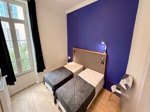 A room with two single beds, a window with curtains, and a blue wall. - Apartment Near Parc Fenestre (La Bourboule)