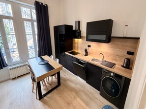 A compact kitchen with a wooden countertop, a built-in washing machine, and a window with curtains. - Apartment Near Parc Fenestre (La Bourboule)