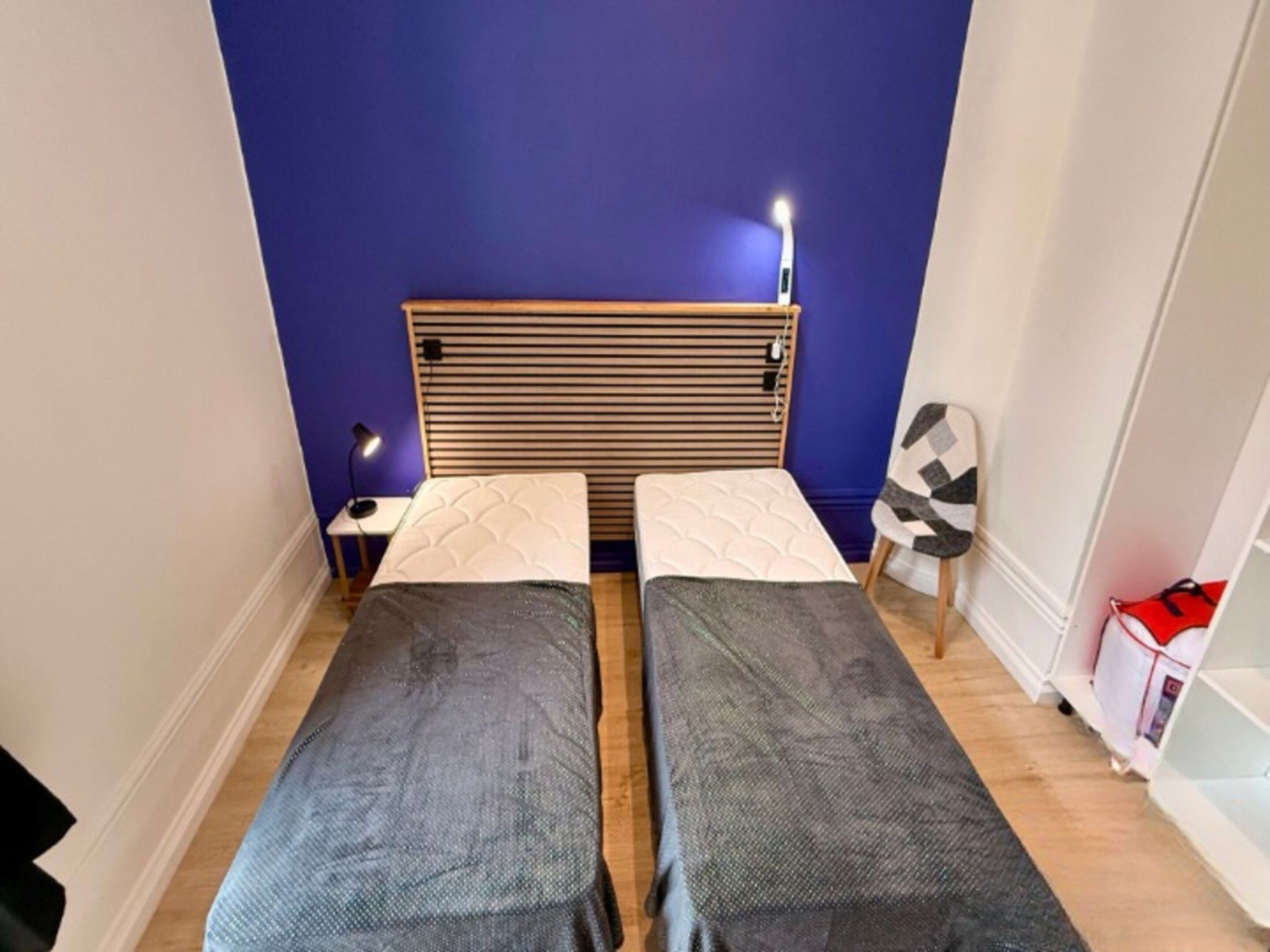 A room with two beds, a headboard, bedside tables, a lamp, and a chair.