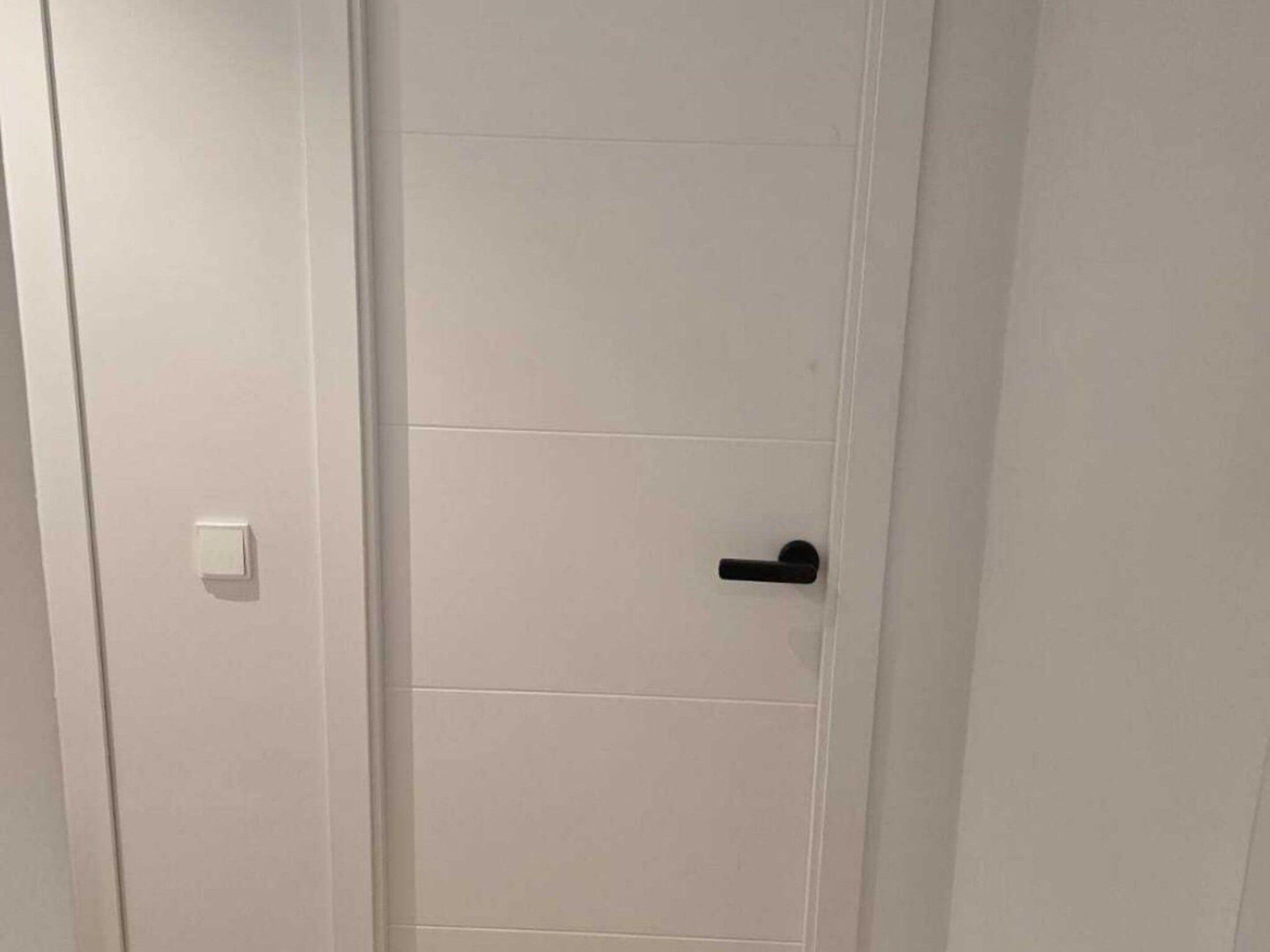 A white door with a black handle and a light switch on the left side.