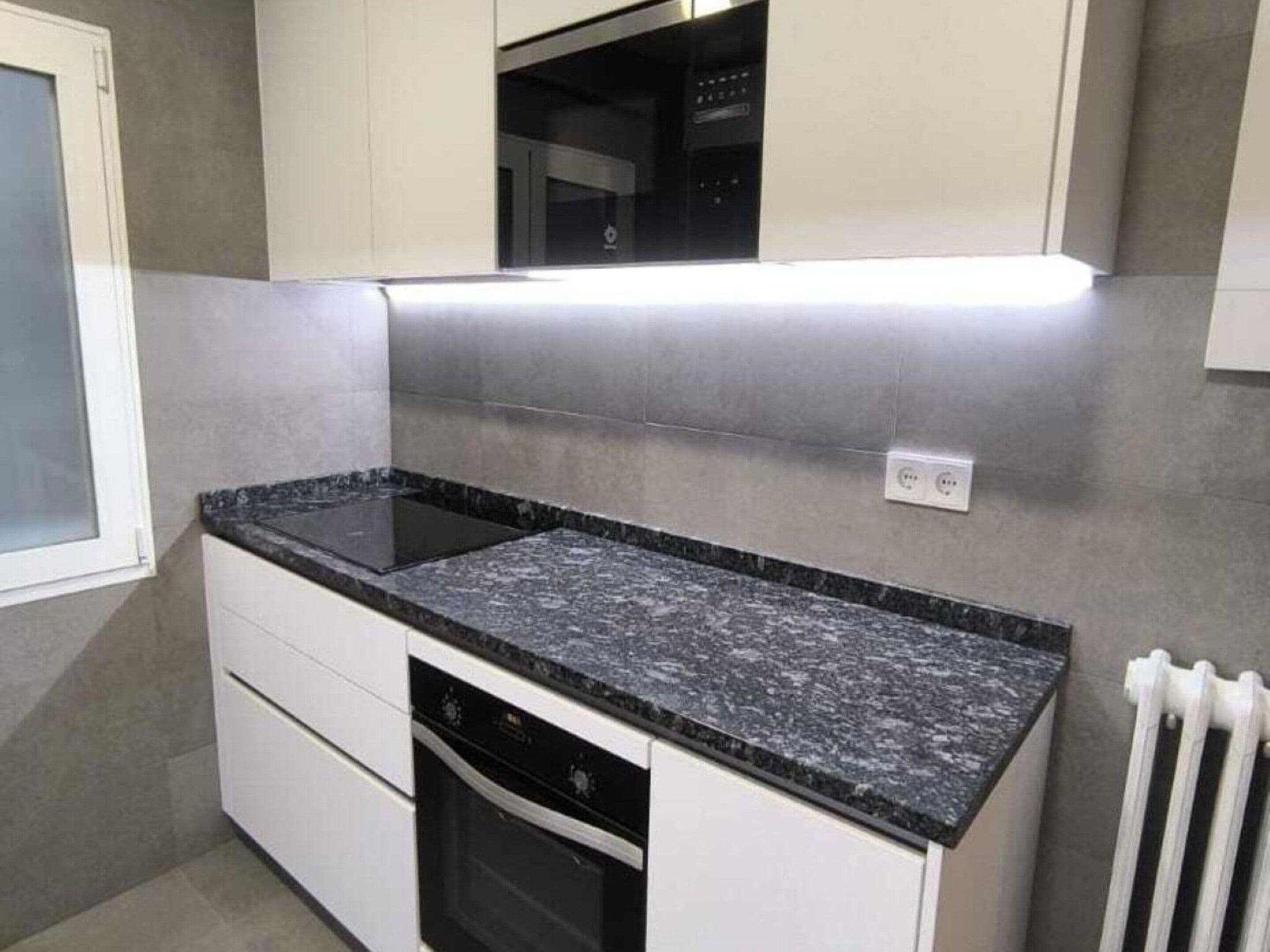 A compact kitchen with a black granite countertop, white cabinetry, and a built-in microwave above the stove.