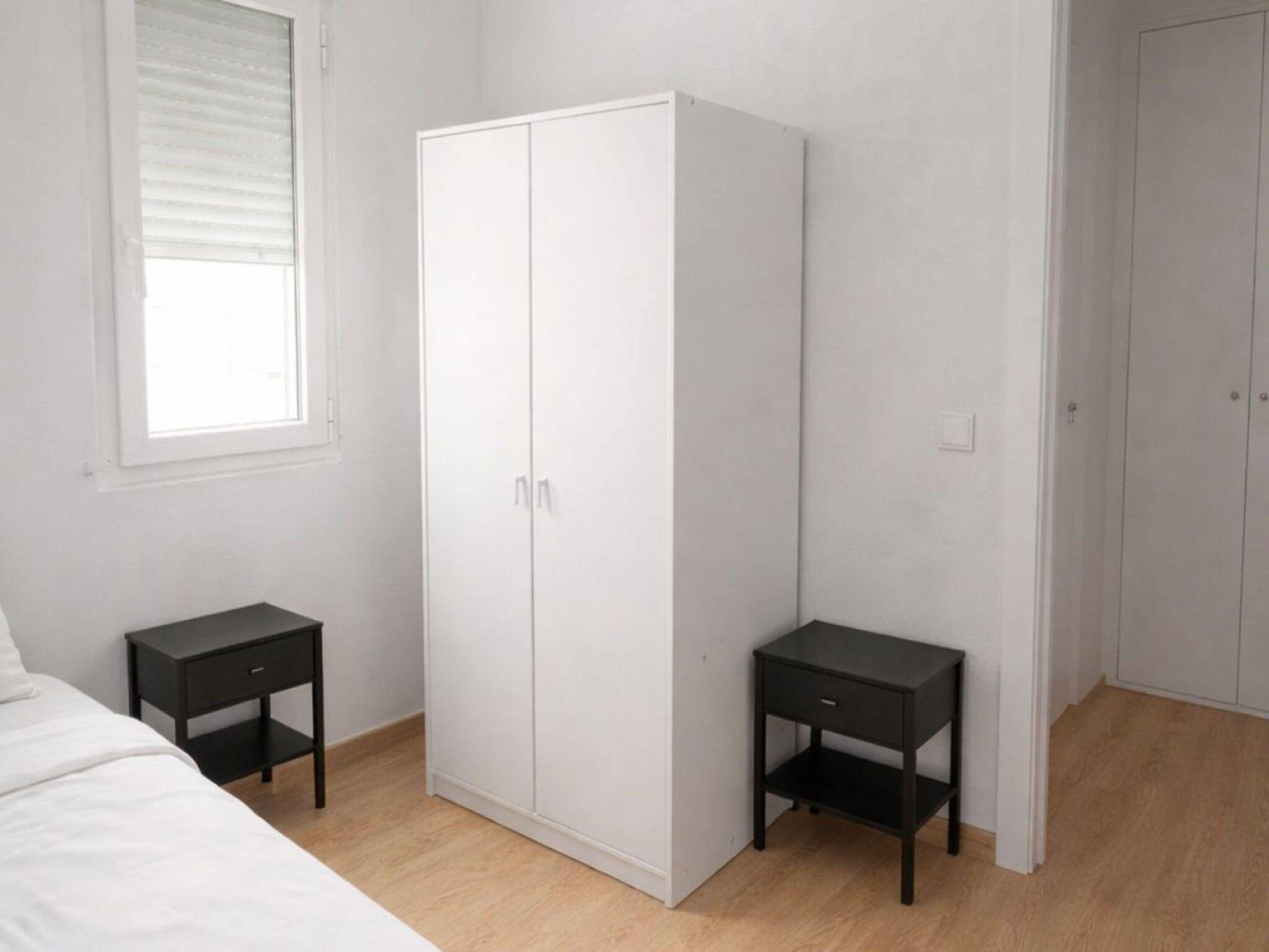 A bedroom with a bed, a wardrobe, two nightstands, and a window with blinds.
