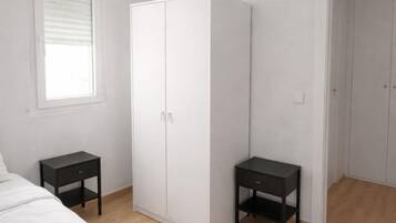A bedroom with a bed, a wardrobe, two nightstands, and a window with blinds.