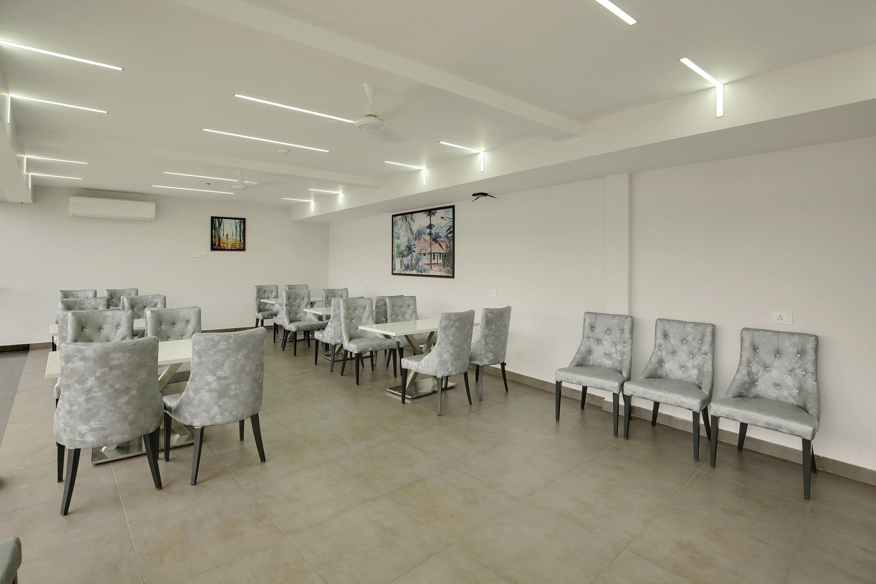 A conference room with multiple tables and chairs, white walls, and ceiling lights.