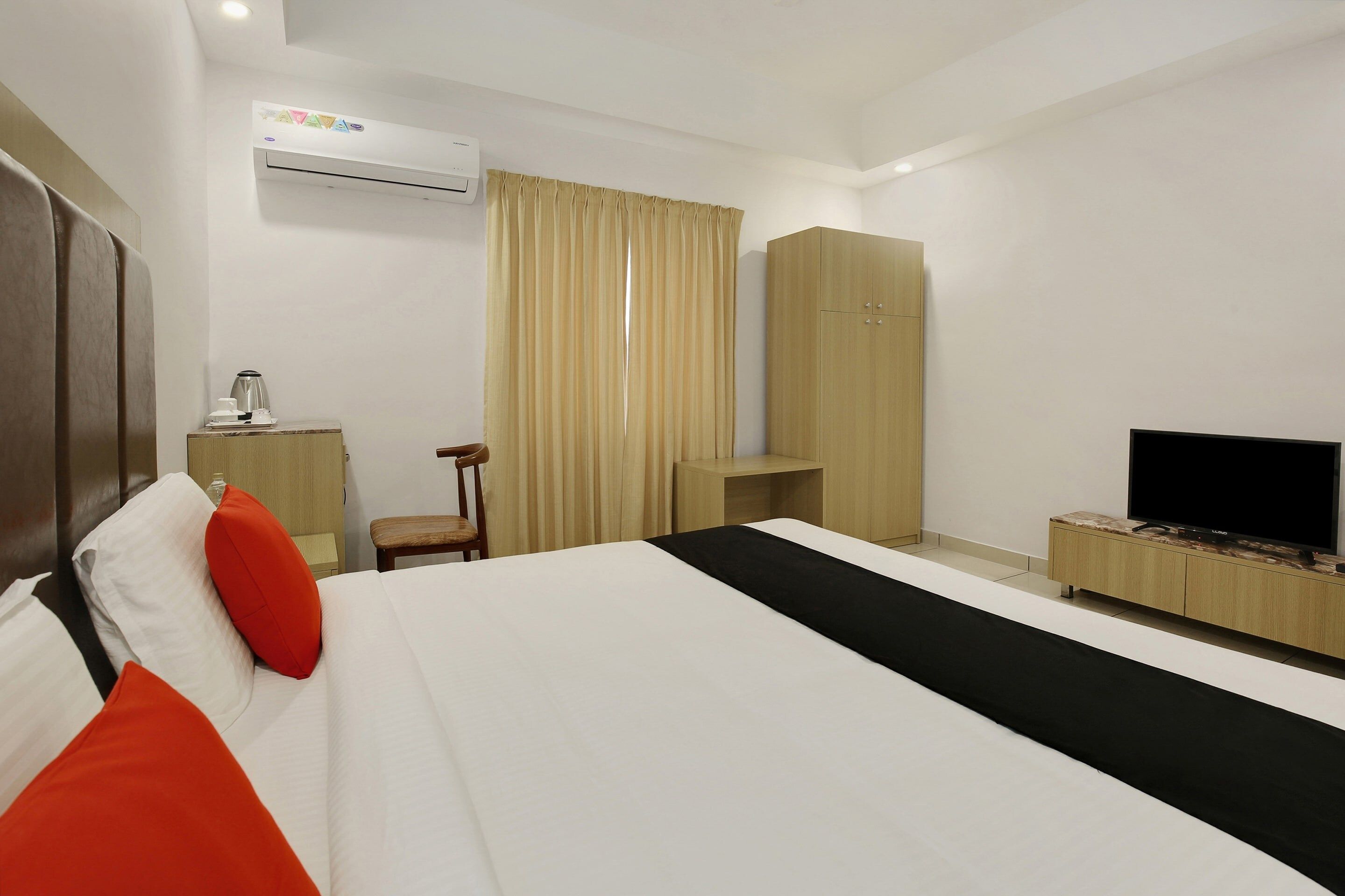 Una habitación de hotel con cama, televisión, armario, escritorio con hervidor y aire acondicionado.