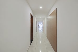 A long, narrow hallway with white walls and a tiled floor, leading to a staircase at the end. - Super Townhouse Edasserys Kalamassery (Kanayannur)