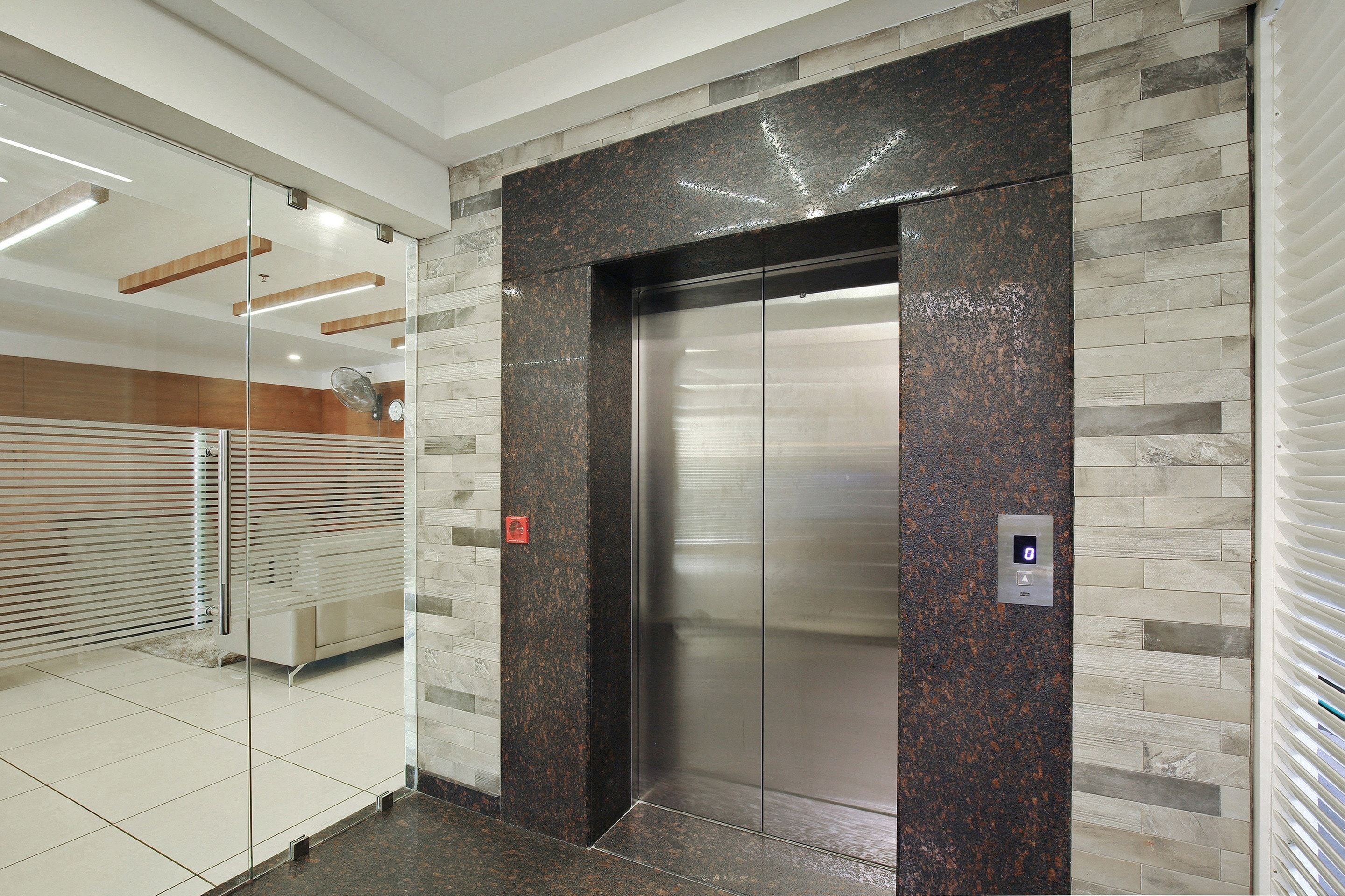 An elevator with a metallic finish, flanked by walls with a mix of stone and wood textures, and a glass partition on one side.