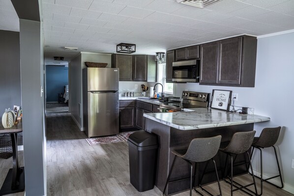 A modern kitchen with dark cabinetry, stainless steel appliances, and a marble countertop.