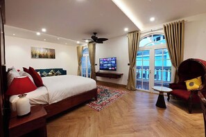 Een hotelkamer met een bed, een televisie, een balkon met gordijnen en een plafondventilator.