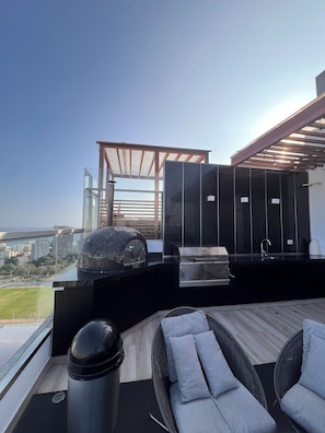 A modern outdoor kitchen with a grill, a seating area with cushions, and a view of the cityscape. - 1 Loft | Pool & Hot Tub | Barranco (Barranco)