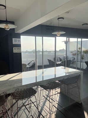A modern dining area with a glass table and metal chairs, large windows with a view of the water, and a sign indicating a maximum capacity of 21 people. - 1 Loft | Pool & Hot Tub | Barranco (Barranco)