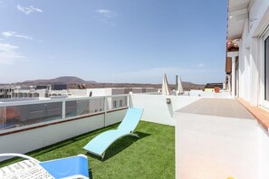 A rooftop terrace with a slide, a pool, and a view of distant hills. - Apartment Near Las Cavellinas Beach (La Oliva)