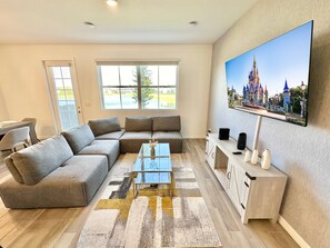 Un salon moderne avec un canapé d’angle, une table basse en verre et un téléviseur à écran plat fixé au mur.