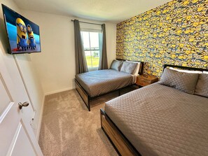 Een hotelkamer met twee bedden, een televisie aan de muur en behangpapier met Minion-thema.