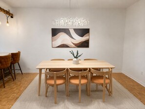 A dining area with a wooden table, six chairs, a chandelier, and a wall-mounted abstract painting. - Adorable Two Bedroom Plateau Montréal Gem with Office Near Parc La Fontaine (Montréal)