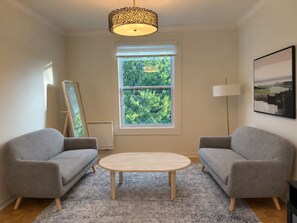 A modern living room with two grey armchairs, a round wooden coffee table, a floor lamp, and a large window with a view of greenery. - Adorable Two Bedroom Plateau Montréal Gem with Office Near Parc La Fontaine (Montréal)