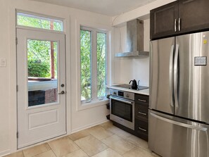Eine Küche mit einem Edelstahlkühlschrank, einem Backofen und einem Fenster mit Blick auf Grünflächen.