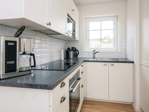 A modern kitchen with white cabinetry, a built-in oven, a coffee maker, and a window providing natural light. - 4 Star Holiday Home in Laeso (Læsø)