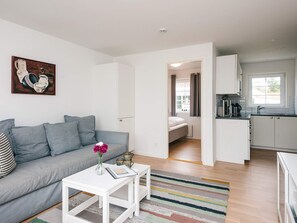 A compact living space with a grey sofa, a white coffee table, and a kitchen area with a microwave and kettle. - 4 Star Holiday Home in Laeso (Læsø)