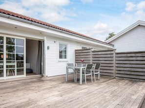 A wooden deck with a table and chairs, a sliding glass door, and a white building with a red-tiled roof. - 4 Star Holiday Home in Laeso (Læsø)