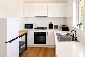 A modern kitchen with white cabinets, a microwave, a stove, an oven, a sink, and a window with a view. - Beach Retreat & City Views (Henley Beach South)