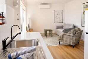 A modern kitchen with a stainless steel sink, a small table, and a grey sofa in a living area. - Beach Retreat & City Views (Henley Beach South)