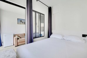 Ein modernes Hotelzimmer mit einem Bett, einer Sitzecke inklusive Sofa, einem kleinen Tisch und einem Fenster mit Vorhängen.