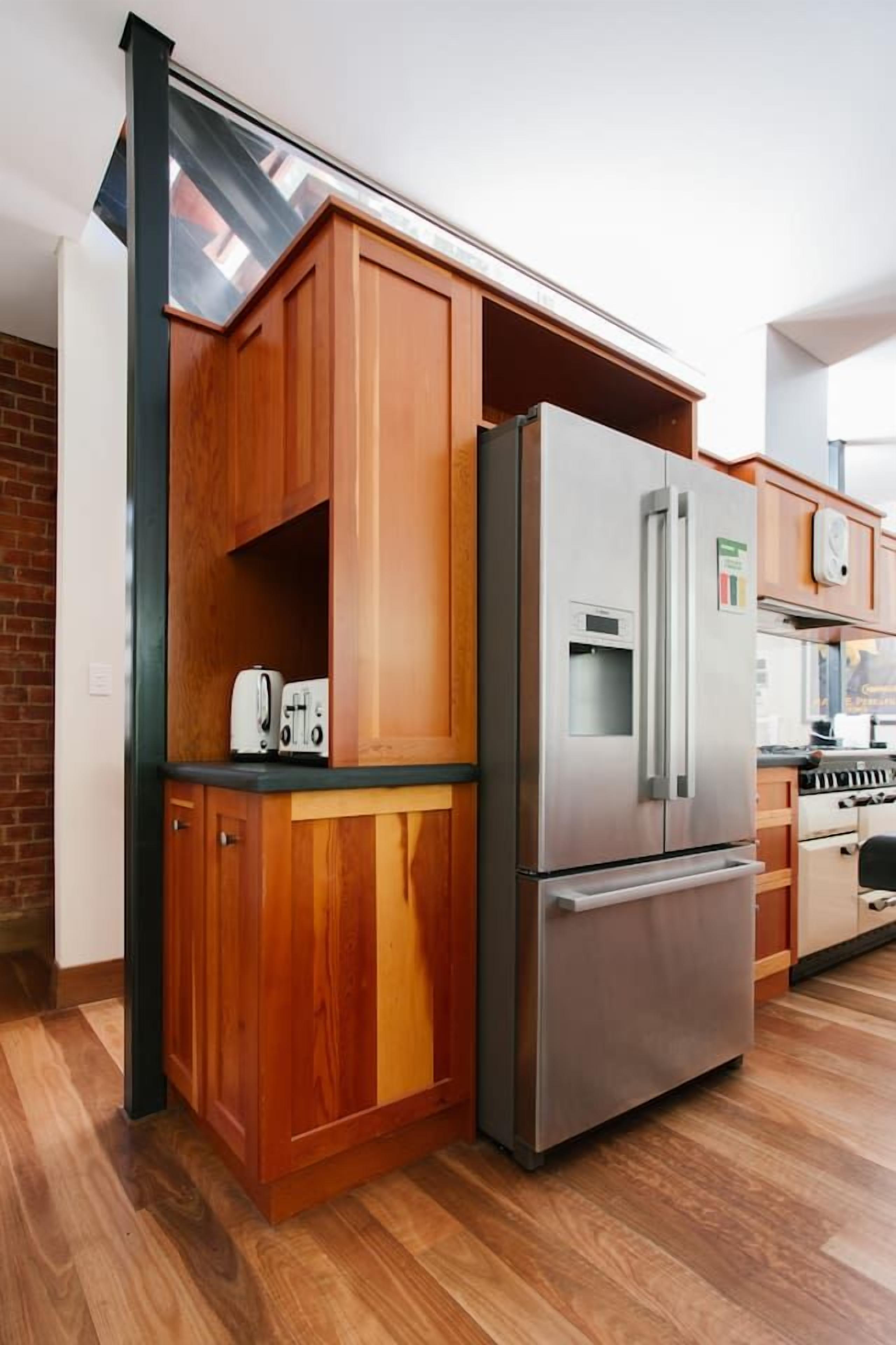 A compact kitchen with wooden cabinets, a stainless steel refrigerator, and a built-in oven.