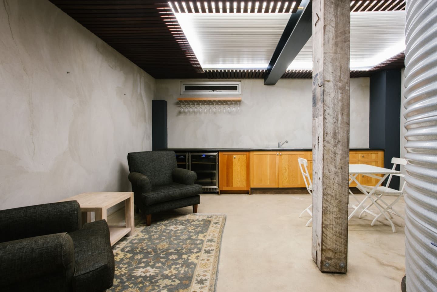 A modern interior with a sofa, a small table, a patterned rug, and a kitchen area with wooden cabinets and a white countertop.