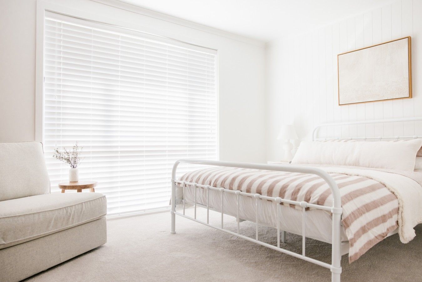 A minimalist bedroom with a bed, a bedside table, and a window with blinds.