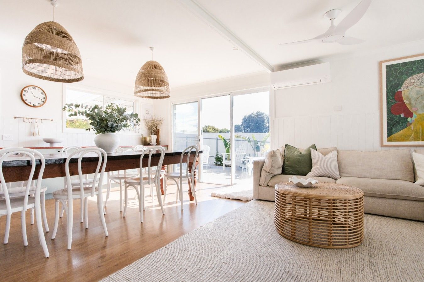 Een moderne woonkamer met een bank, een eethoek met stoelen, een groot raam en een plafondventilator.