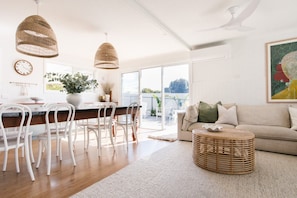 Een moderne woonkamer met een bank, een eethoek met stoelen, een groot raam en een plafondventilator.