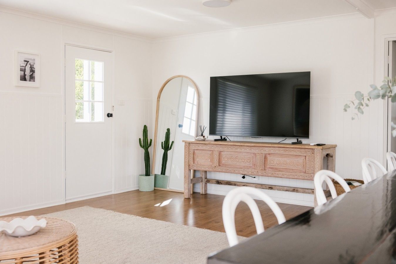 Een eethoek met een houten tafel, witte stoelen, een grote flatscreen televisie en een rustieke houten kast.